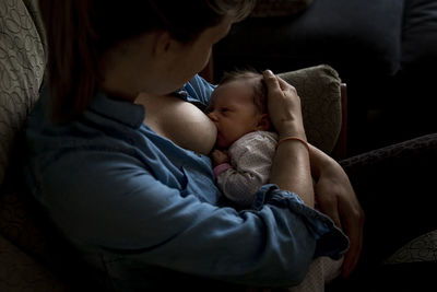 High angle view of mother breastfeeding newborn daughter while sitting on sofa at home