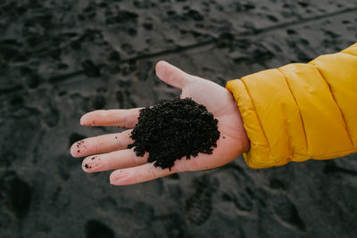 Man in a yellow jacket holding black sand from the beach in the palm of his hand