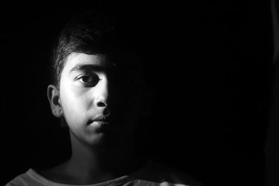 Monochrome photograph of a teenage boy against a black background with one side of the face lit