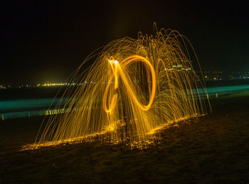 Illuminated ferris wheel on beach against sky at night