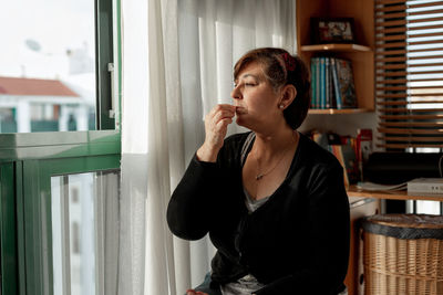 Young woman looking away while sitting on window at home