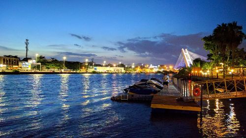 Boats sailing on river by illuminated city against sky at night