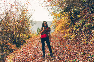 Full length of woman photographing while standing in forest during autumn