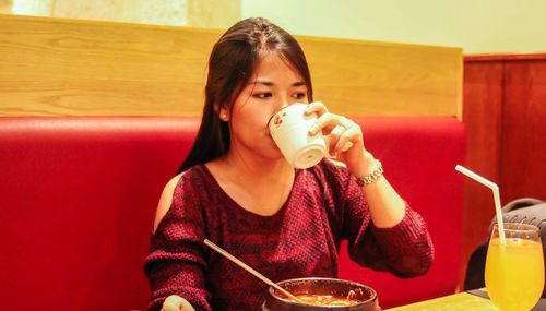 Young woman having drink on seat at restaurant