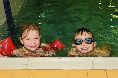 Chidren in public pool. girl wears armband floats and boy with swimming goggles.