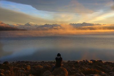 Rear view of man looking at sea against sky during sunset