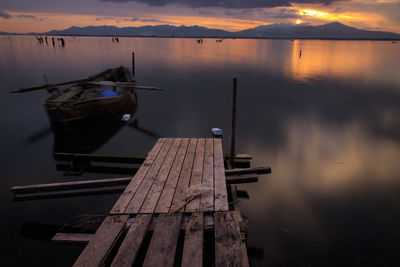 Boat moored in lake against sky during sunset