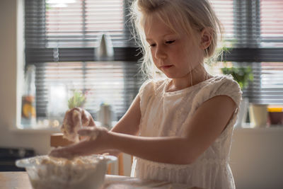 Cute girl mixing food in bowl on table at home