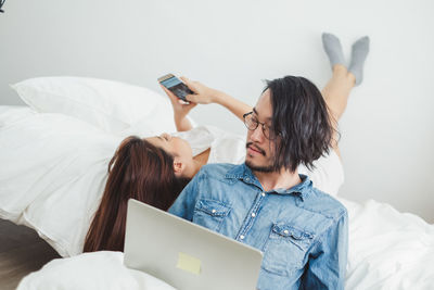 Young woman using mobile phone while sitting on bed at home