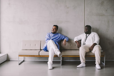 Full length of male healthcare workers sitting on sofa taking break at hospital