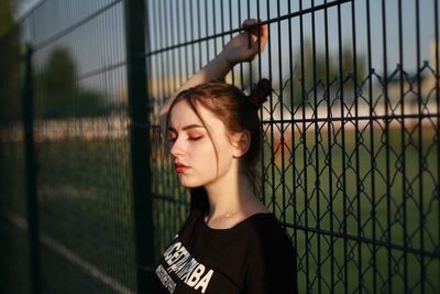 Young woman standing by fence outdoors