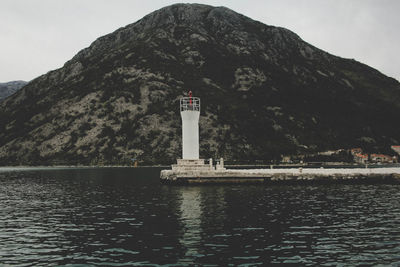 Lighthouse amidst buildings and mountains against sky