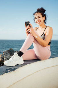 Young woman using mobile phone while sitting on beach