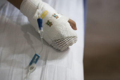 Cropped image of child with hand wrapped in bandage on bed at hospital