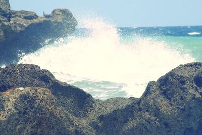 Waves splashing on rocks at shore against sky