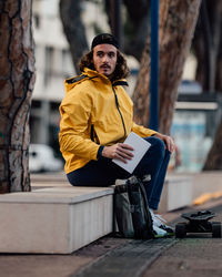 Full length of man looking away while sitting by tree