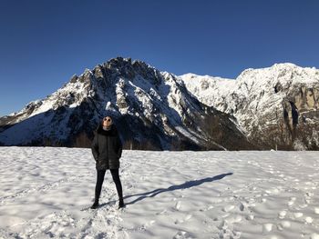 Woman standing on snow covered land against clear sky