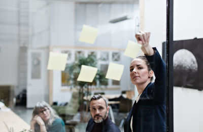 Confident businesswoman explaining adhesive notes to coworkers at office