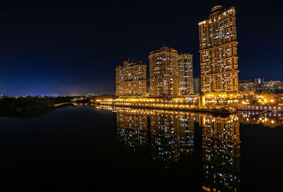 Illuminated buildings by river against sky at night