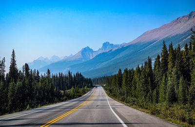 Road amidst trees and mountains against sky