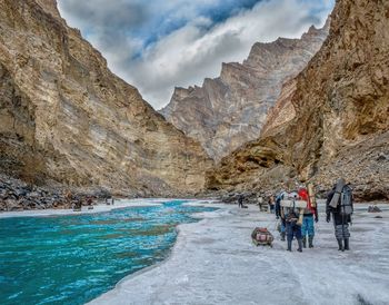 People hiking on ice by mountain against sky