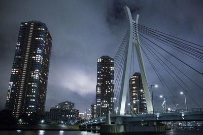 Low angle view of illuminated bridge against buildings at night