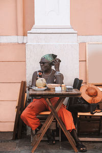 Cool mature african american male in sunglasses and bracelets sitting at urban cafeteria table with coconut beverage