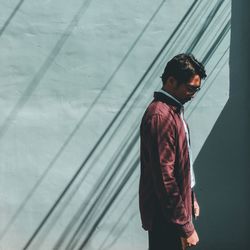 Young man looking down while standing against wall