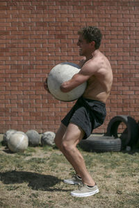 Side view of shirtless disabled male athlete carrying atlas stone while standing on field during sunny day