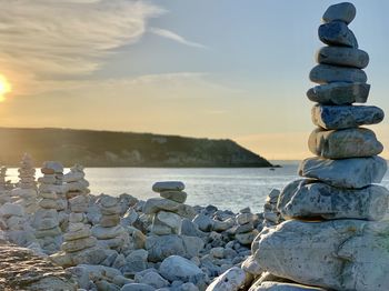 Stack of stones on beach against sky during sunset