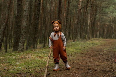 Toddler baby boy in bear bonnet standing in the woods