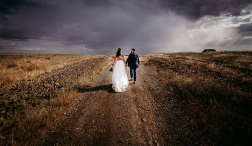 Rear view of friends standing on field against sky