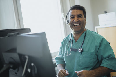 Portrait of cheerful doctor wearing headset sitting at hospital