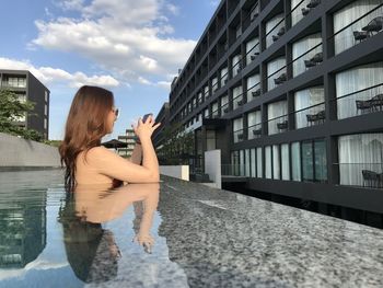 Woman standing by swimming pool against sky
