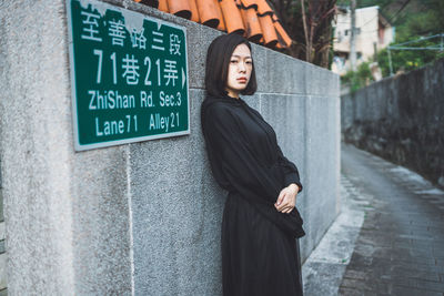 Portrait of young woman standing against wall