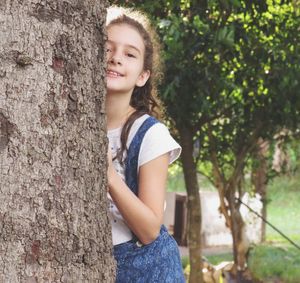 Portrait of smiling girl holding tree trunk