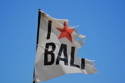 Low angle view of flag on sign against clear blue sky