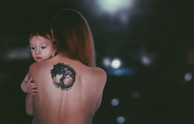 Rear view of shirtless woman holding baby