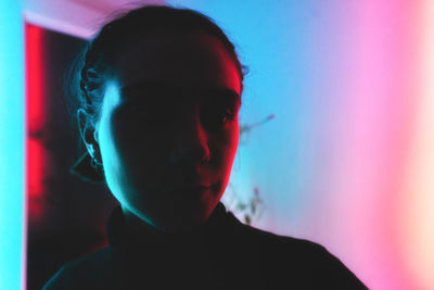 Close-up portrait of woman standing against illuminated wall