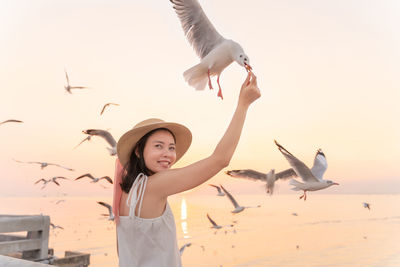 Smiling woman feeding seagull against clear sky during sunset