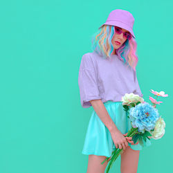 Portrait of woman holding flowers standing against colored backgrounds