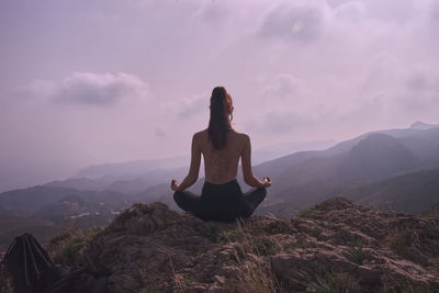 Woman meditating on mountain against sky