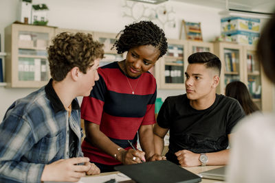 Female professor discussing with male students while standing in classroom