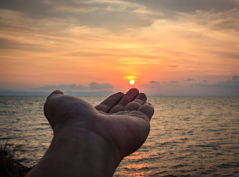 Midsection of person against sea during sunset