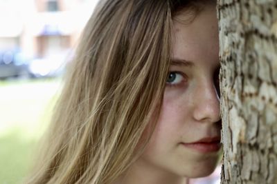 Close-up portrait of beautiful young woman standing by tree trunk