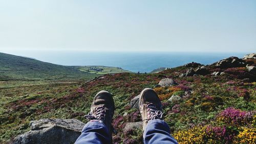 Low section of man standing on cliff by sea against clear sky