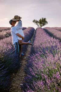 Side view of couple standing on flowering field against sky