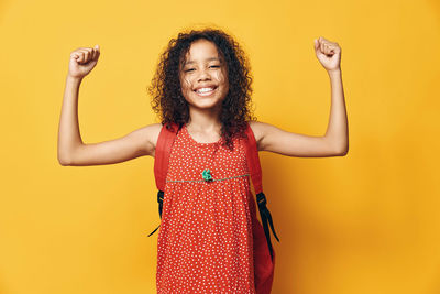 Portrait of young woman standing against yellow background