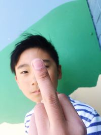 Portrait of young man showing obscene gesture against wall