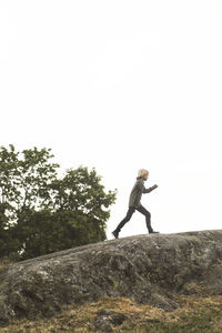 Full length of girl running on rock formation against clear sky